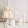 Elegant și armonios, acest set este alegerea ideală pentru un botez de poveste. Include o rochiță delicată în nuanță ivoire, realizată din muselină triplustrat, accesorizată cu volan din dantelă brodată și detalii rafinate ce oferă un aer clasic. Ținuta este completată de botoșei asortați și o bonetă elegantă, perfect coordonate cromatic. Setul conține și un trusou de botez din bumbac, format din 7 piese esențiale, atent lucrate pentru confortul bebelușului, alături de o lumânare de botez decorată manual, în ton cu întreaga tematică.